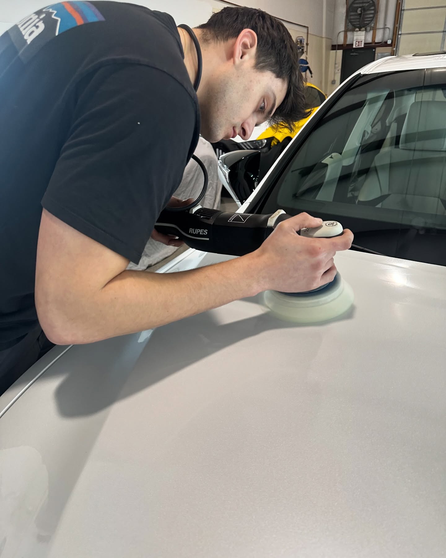 Machine polishing the hood of a white vehicle at the Detail Tech shop