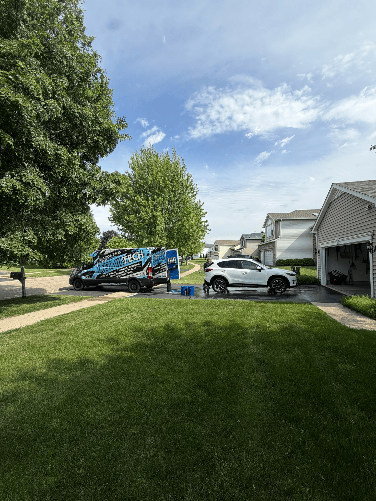 Detail Tech mobile detailing van hand washing a white SUV in a customer's driveway