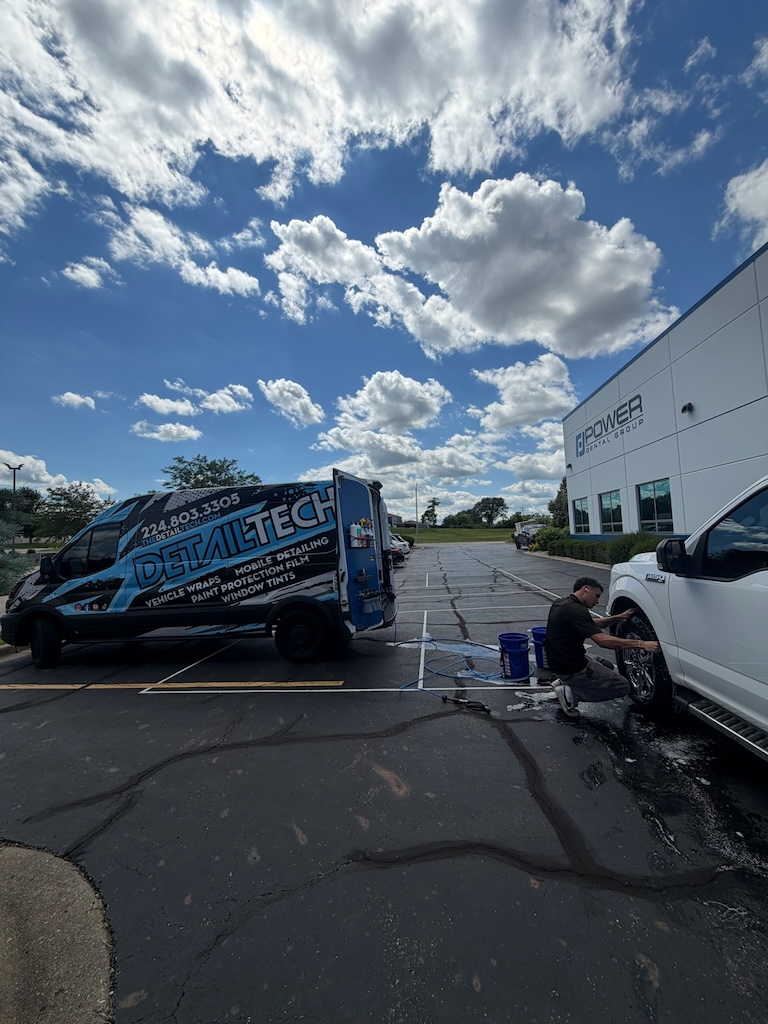 Detail Tech technician cleaning the wheels of a white pickup truck on site