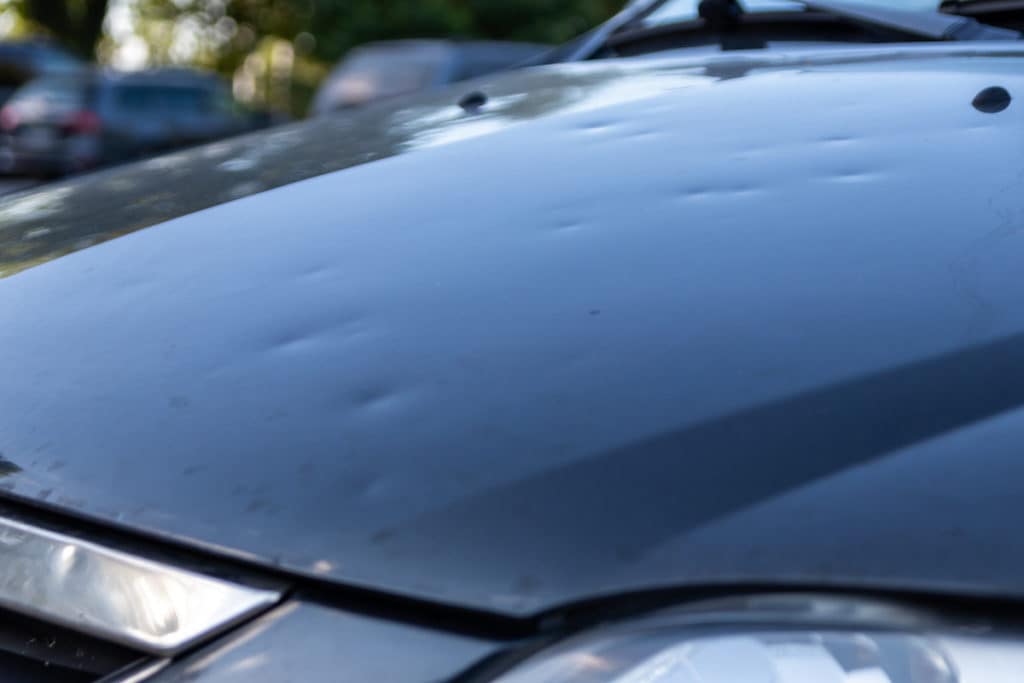 Minor hail dents across a car hood before paintless dent repair at Detail Tech