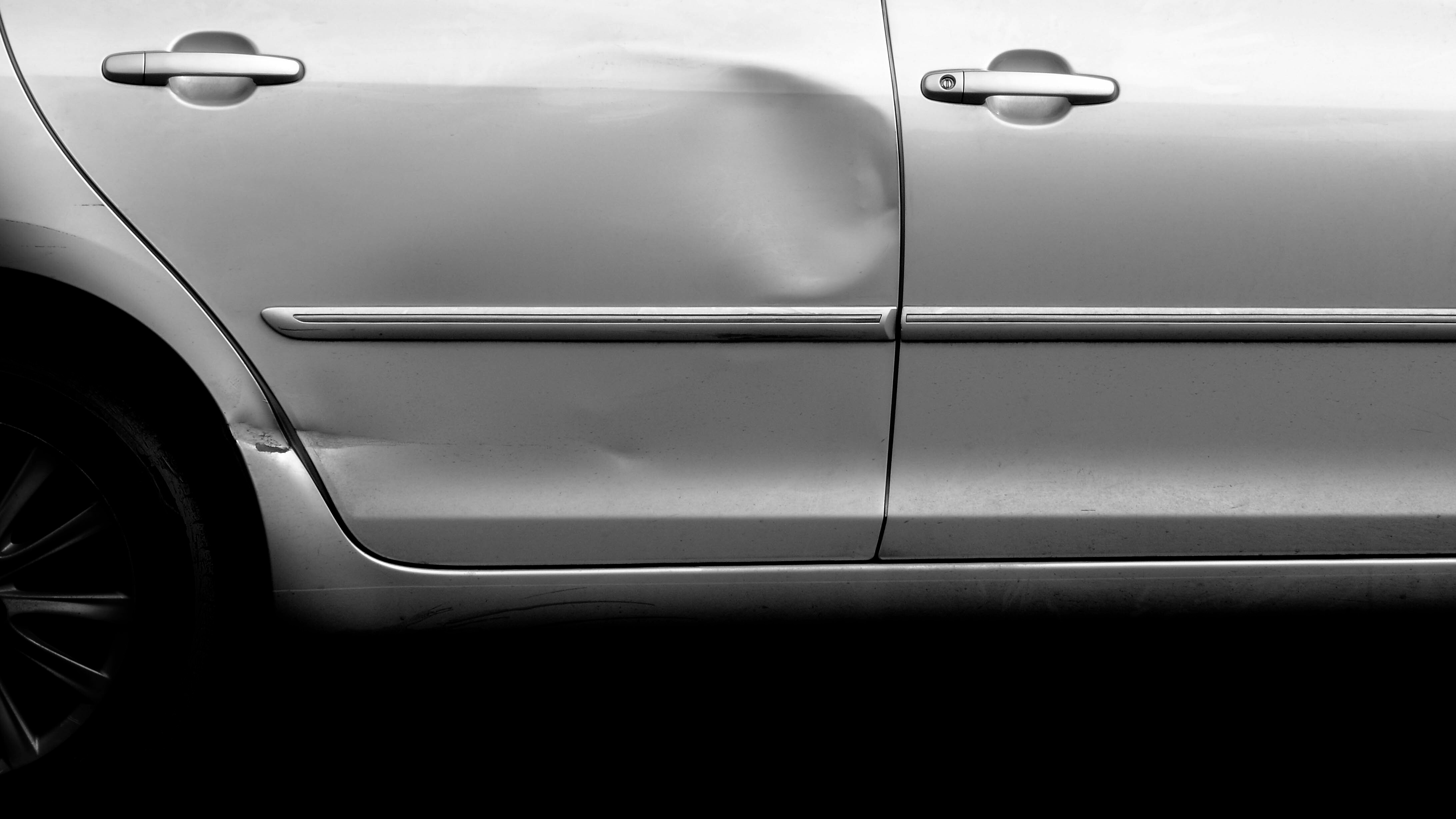 Large dent across the door panel of a silver car before paintless dent repair at Detail Tech