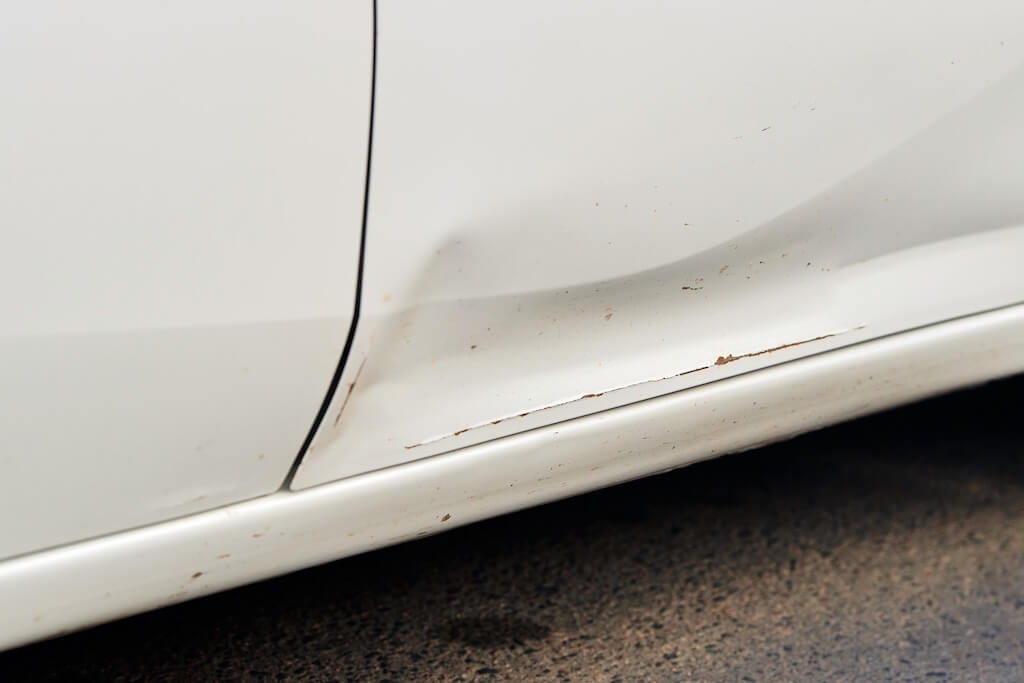 Crease and minor dent along the lower door panel of a white car