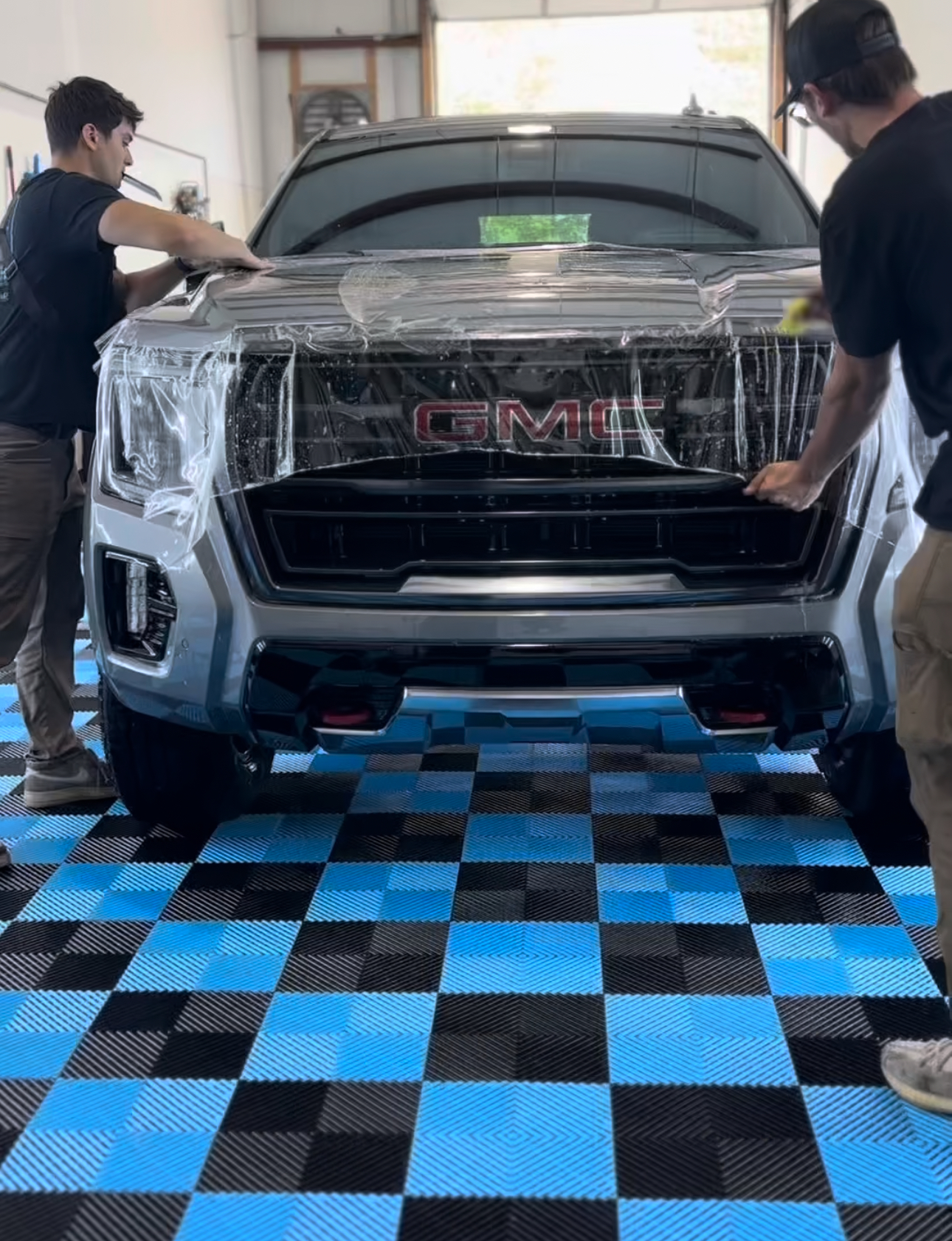 Detail Tech installers applying paint protection film to the front end of a GMC