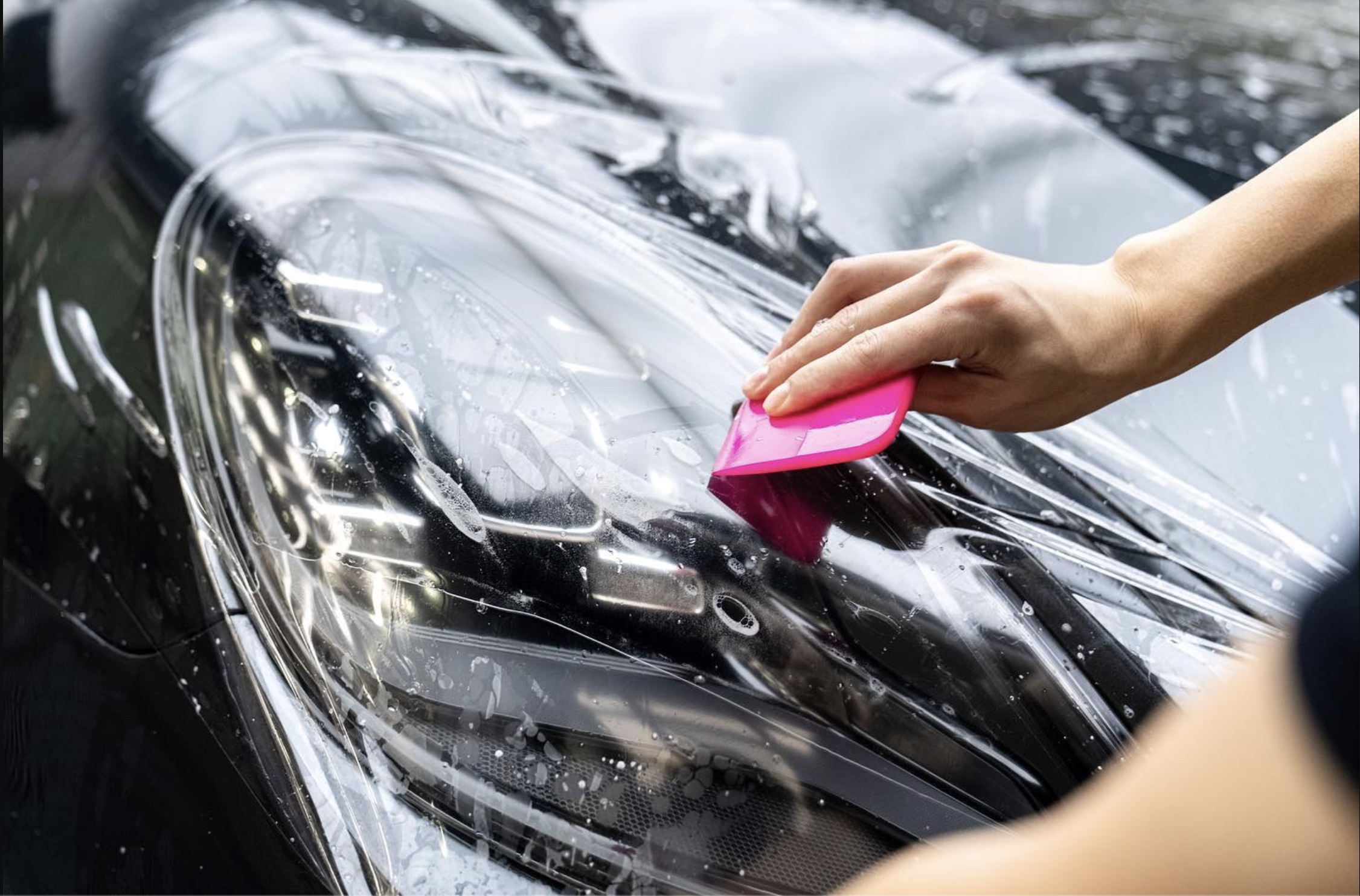 Smoked tint film being squeegeed onto a headlight at Detail Tech