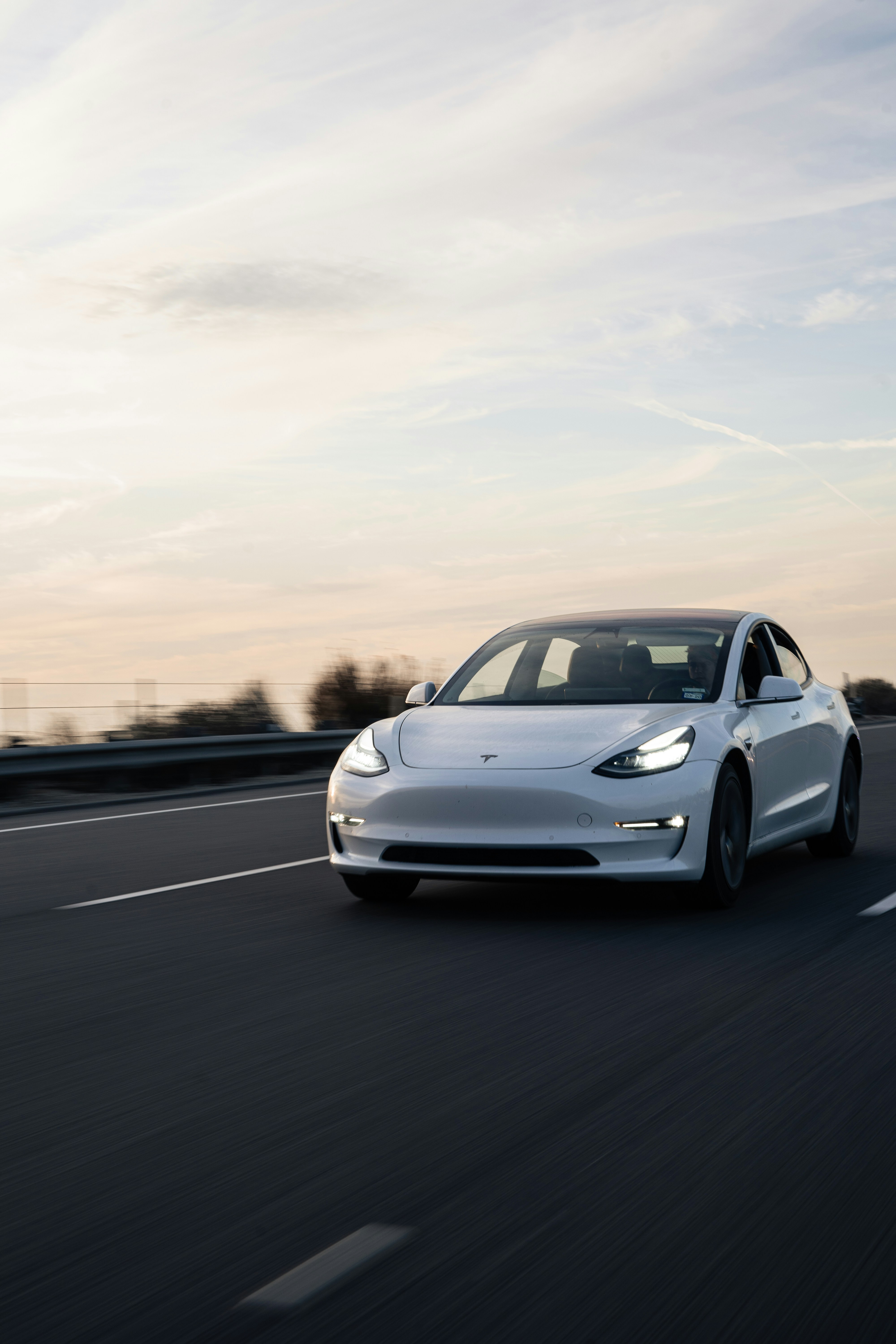 White Tesla Model 3 driving on the highway at dusk