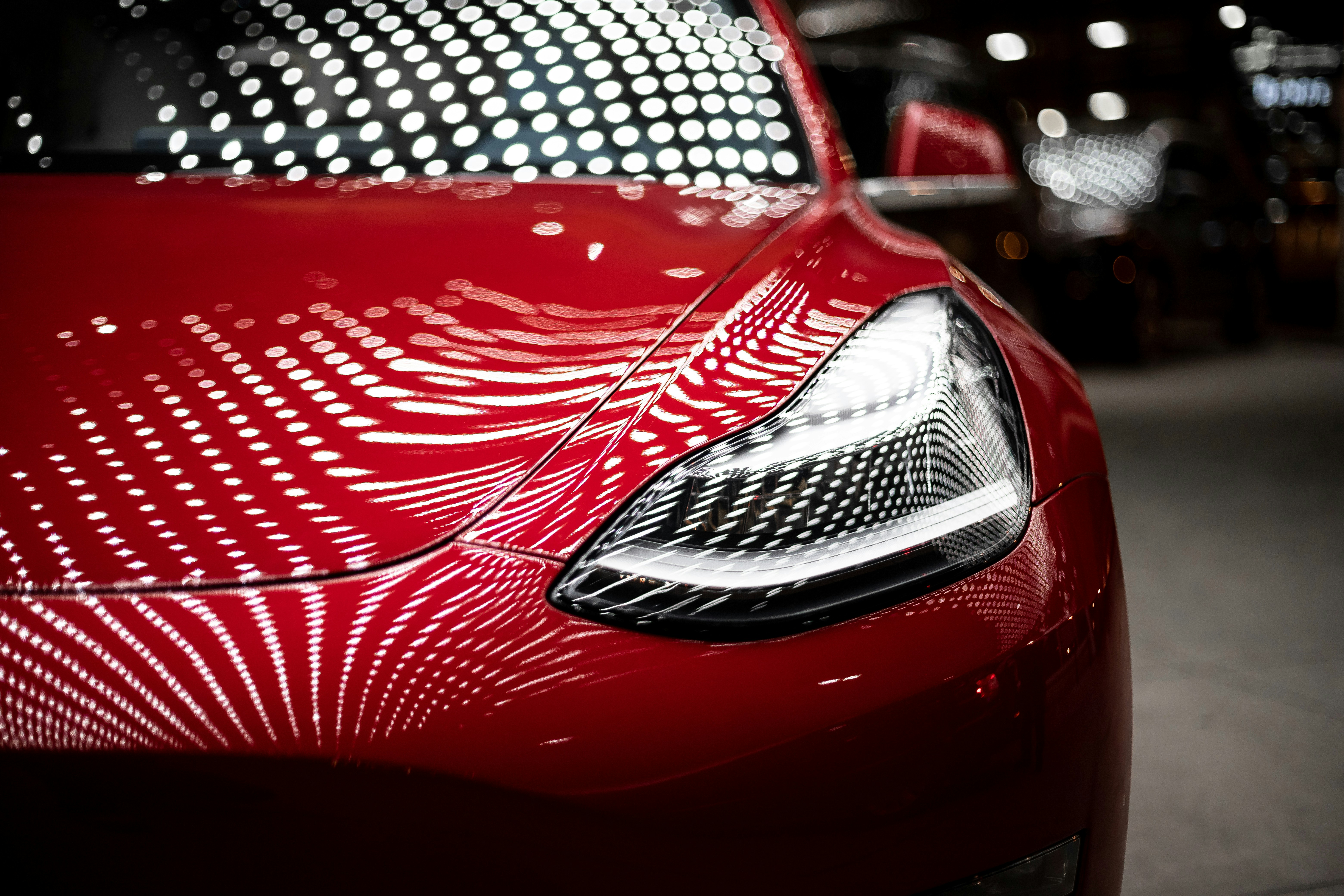 Glossy red Tesla with ceramic coating reflecting showroom lights